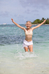 Girl having fun splashing in the ocean, water splashes, white sand, blue water, exotic summer vacation