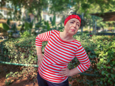 A mature determined woman in a red bandana does side bends during her daily gymnastics in a green park, battling the effects of chemotherapy with a resolve to defeat cancer.