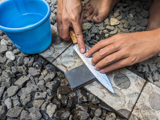 Closeup man hands sharpen knife on whetstone sharpener or grindstone in outdoors. Concept,...