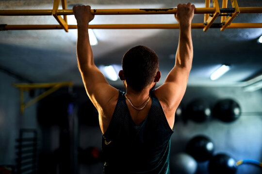 Back view of a strong man doing pull ups in a gym