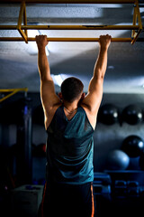 Back view of a strong man doing pull ups in a gym