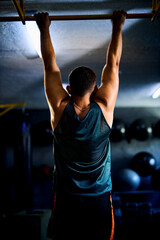 Back view of a strong man doing pull ups in a gym
