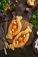 Khachapuri pie in Ajarian. Open pie with cheese and egg on wooden board with ingredients, basil, cilantro, egg yolk and spices. Traditional Georgian cuisine. Top view. Copy Space.