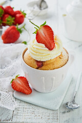 Strawberry banana mug cake. Fresh homemade cake in mug with strawberry, banana and whipped cream in white rustic ceramic mug cup on white wooden table background. Healthy breakfast cooked in microwave