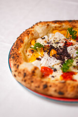 Pizza napoletana gourmet con mozzarella, pomodori rossi, pomodori gialli, prezzemolo e cacao amaro servita in una pizzeria