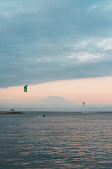 Extreme beautiful sport. Two men ride in the ocean on kite surfboards with sails and do tricks. Against the backdrop of mountains and a volcano during a colorful sunset.