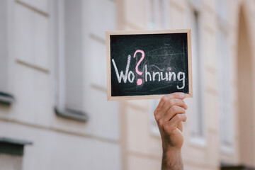 Person hält Tafel mit Schrift Wohnung innerhalb einer Stadt hoch 