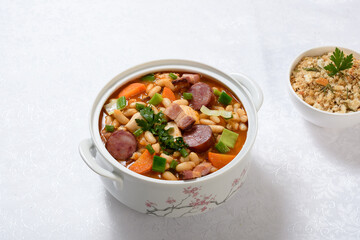 A bowl of chicken cassoulet and spicy breadcrumbs on a white table