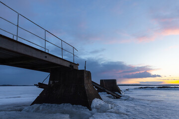Broken pier is under sunset sky, coastal winter landscape