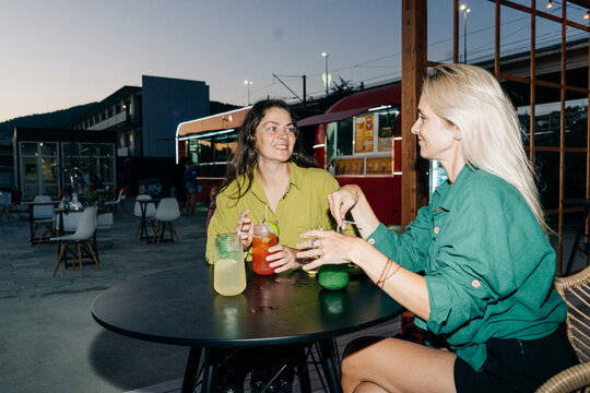 Two women friends sitting at a table in a cafe outside drinking cool drinks.