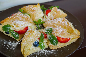 Homemade white cream puffs with mascarpone and sour cream, decorated with red strawberries and blueberry leaves with green mint leaves inside. 