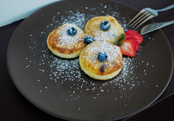 Easy breakfast in the form of golden cheesecakes with homemade cottage cheese with raisins in the middle , and decorated with blue blueberries and pieces of red-pink strawberries on top. 