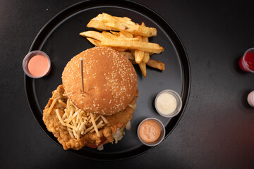 Crispy chicken burger on black background. Tomato, lettuce, chicken burger, sauces and fries.