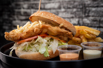 Crispy chicken burger on black background. Tomato, lettuce, chicken burger, sauces and fries.