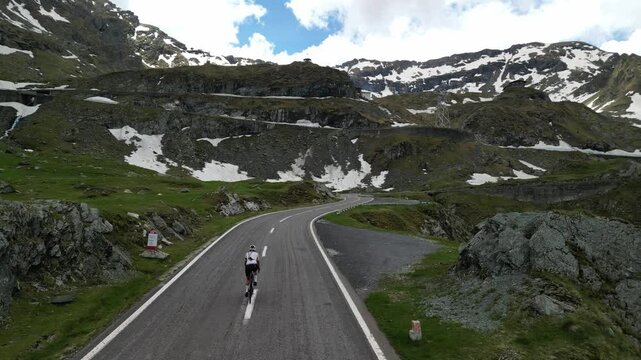 Aerial drone shot of female cyclist pushing pedals on bicycle up an asphalt road in mountains with amazing view. Cycling on a serpentine road.  Sport motivation. Active sport. Transfagarasan, Romania