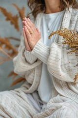 Woman in cozy knitwear with clasped hands in prayer, surrounded by autumnal dried foliage. Mindfulness, meditation, autumn style, cozy living, fashion, spiritual practice, relaxation.