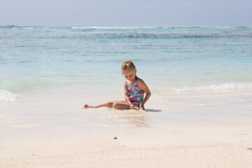 A girl plays with sand, a child builds a castle from sand, white sand, ocean in the background, summer vacation