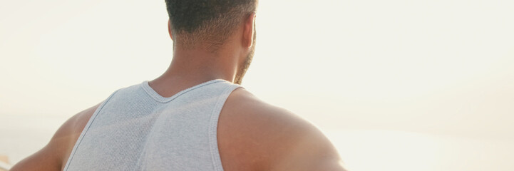 Fototapeta premium Young bearded male fit athlete standing on the embankment looking at the sea.