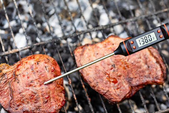 Close-up shot of digital meat thermometer inside grilled steak on barbecue showing the right temperature for Medium doneness