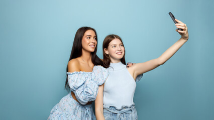 two women together wears blue casual clothes do selfie shot on mobile cell phone isolated on plain...