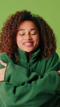 Young woman in cozy sweater hugging herself on a green screen background
