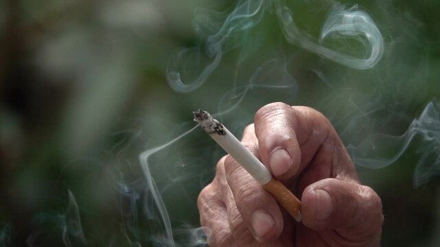 A person holding a cigarette and smoking it. The smoke is thick and billowing, and the person's hand is holding the cigarette