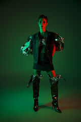 Fototapeta premium Woman in denim jacket and knee-high boots stands in studio, lit by green and red neon lights