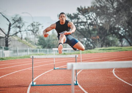 Hurdles, fitness and man sprinting on track at stadium training for race, competition or marathon. Energy, jump and male athlete running by equipment for cardio workout or exercise at sports arena.