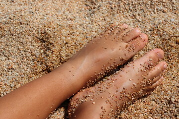 A person's feet are in the sand, with the sand covering their toes