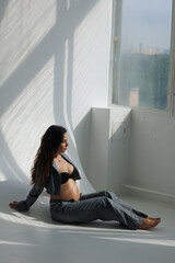 A beautiful pregnant brunette woman in a cropped gray stylish suit on a white background in the studio. A pretty girl with a bare stomach in a fashionable suit is sitting on wooden staircase barefoot.