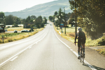 Fototapeta premium A woman cyclist training on a lonely road on a sunny day wearing a black jersey and bib shorts and a white helmet.