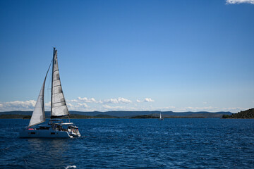 Sailboat sailing on a calm blue sea near an island on a sunny day