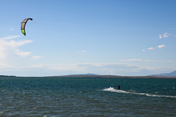 Kitesurfer is riding a wave on a sunny day with blue sky