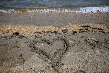 Heart drawn in the sand on a beach being washed away by the ocean waves, representing lost love