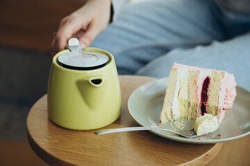 A piece of cake and a green teapot on a table in a cafe, a delicious dessert.
