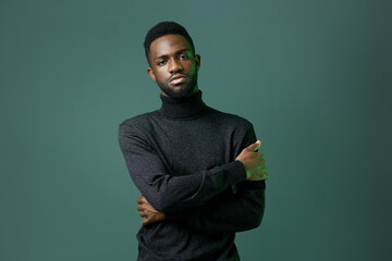 Confident african american man in stylish turtleneck sweater posing against a vibrant green...