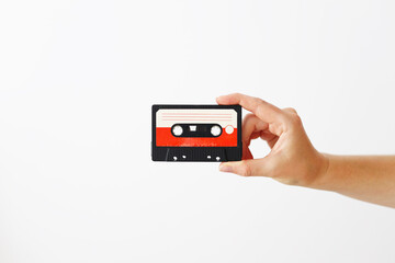 A hand holding a cassette tape. The tape is red and white