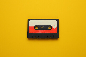 A cassette tape is laying on a yellow background. The tape is old and worn, with a red and white...