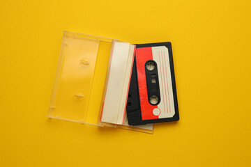 A cassette tape is laying on a yellow surface. The tape is open and the case is still closed