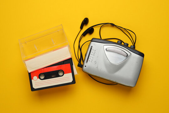 A silver cassette tape recorder sits on a yellow surface next to a pair of headphones. Concept of nostalgia and a longing for simpler times when music was played on cassette tapes
