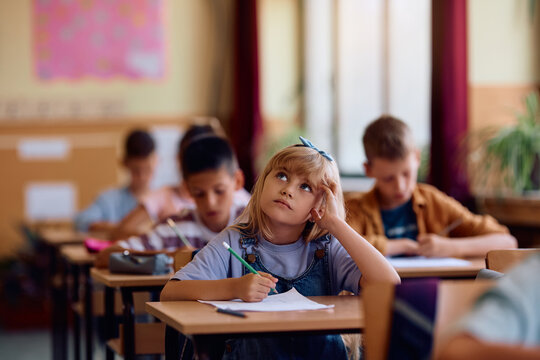 Pensive schoolgirl writing test in classroom. - Powered by Adobe