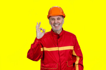 Happy smiling construction worker gives okay gesture sign. Isolated on yellow.
