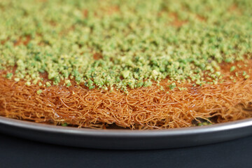 A traditional Arabic or Turkish dessert, Kunafa with pistachio, displayed elegantly on a plain background, highlighting its golden-brown crust and nutty topping.