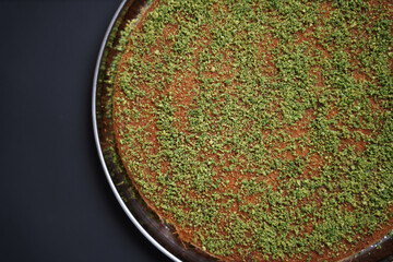 A traditional Arabic or Turkish dessert, Kunafa with pistachio, displayed elegantly on a plain background, highlighting its golden-brown crust and nutty topping.