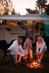 A family cooks sausages on a bonfire near their motorhome in the woods