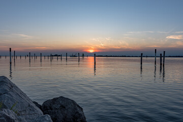 Obraz premium Serene Sunset on the Sea in Grado: Splendid Reflections and Colors Admired from a Rocky Pier.
