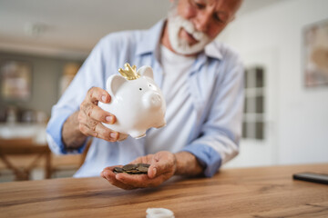 Senior man count money from the piggy bank and save money at home