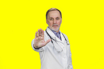 Senior aged doctor wearing stethoscope shows no reject gesture sign with his hand. Isolated on...