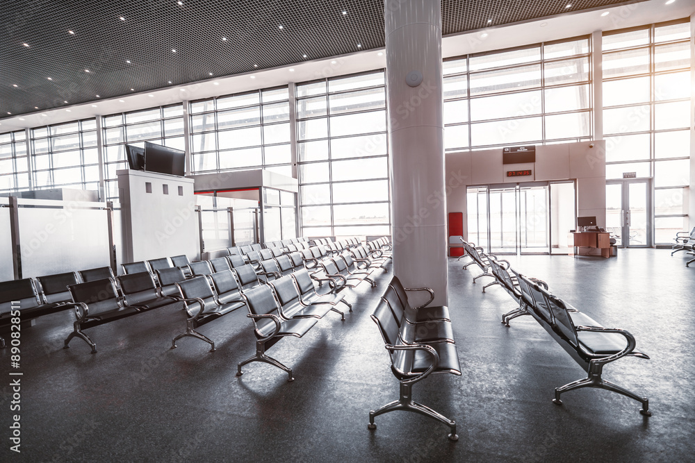 Wall mural A modern, spacious airport waiting hall with rows of black metal seating, large windows allowing natural light to flood the space, and a digital information screens. An empty area ready for passengers