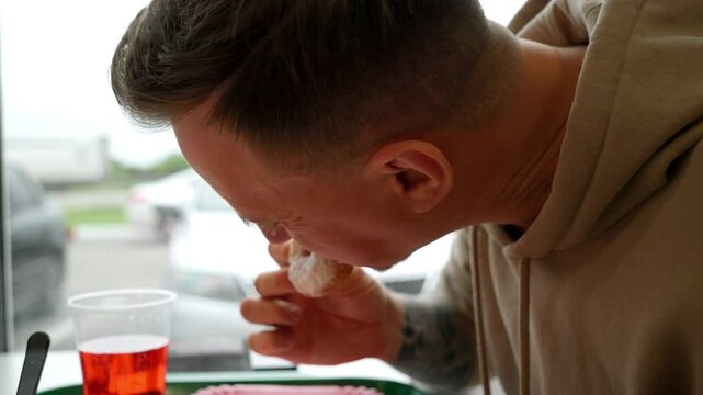 young man in a roadside cafe disgustingly eats donuts with powdered sugar on them. Unhealthy snack while stopping on the highway.